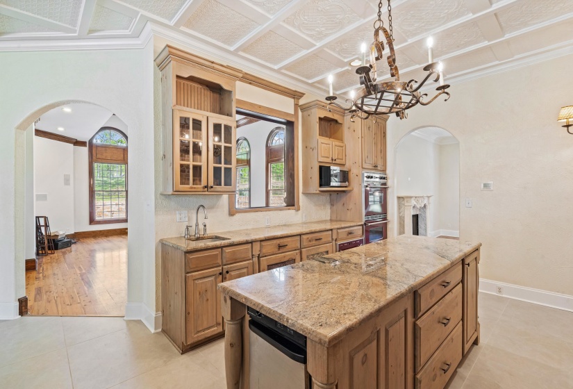 Kitchen with arched walkways, light stone counters, glass fronted cabinets, crown molding, and a chandelier
