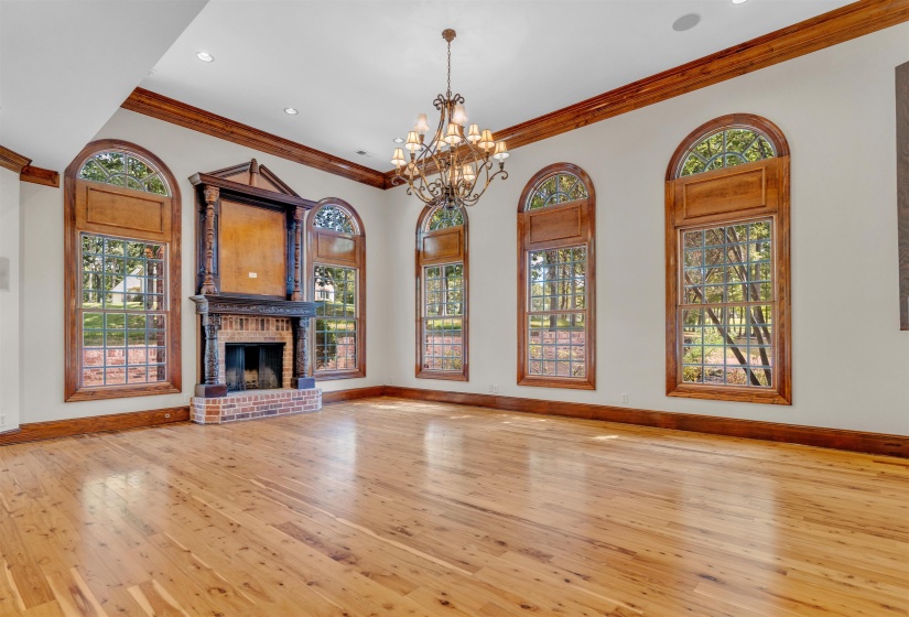 Unfurnished living room with light wood-type flooring, crown molding, healthy amount of natural light, a chandelier, and a fireplace