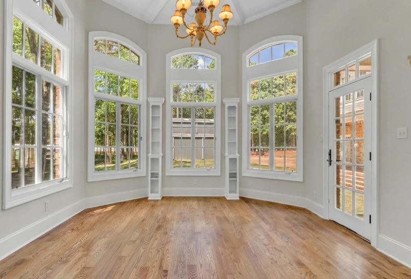 Unfurnished sunroom with suspended lighting, crown molding, and wood finished floors