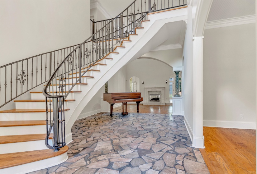 Foyer featuring a high ceiling, a fireplace with raised hearth, ornamental molding, wood finished floors, and stairway