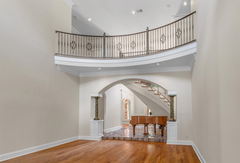 Entryway featuring a towering ceiling, light wood finished floors, ornamental molding, arched walkways, and recessed lighting