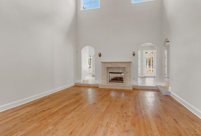 Unfurnished living room featuring a premium fireplace, light wood finished floors, a towering ceiling, and arched walkways
