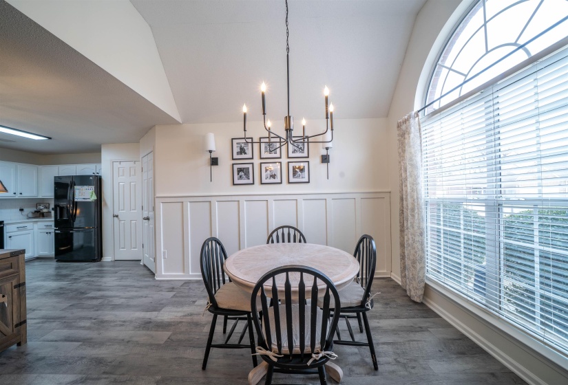 Dining area with a decorative wall, vaulted ceiling, a chandelier, a wainscoted wall, and dark wood-style floors