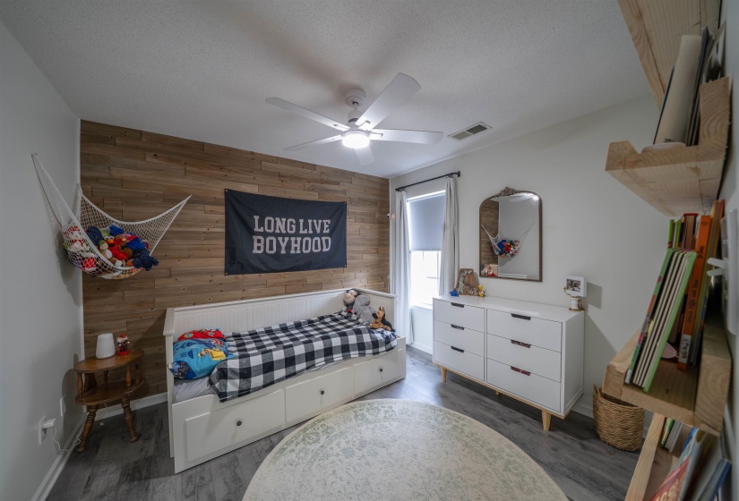 Bedroom with wooden walls, an accent wall, dark wood-type flooring, ceiling fan, and a textured ceiling