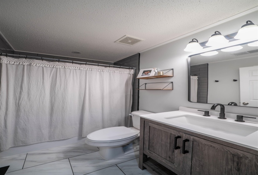 Full bathroom featuring vanity, a textured ceiling, light marble finish floors, shower / bath combination with curtain, and ornamental molding