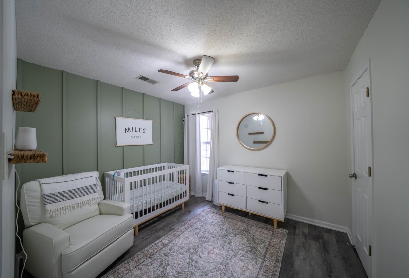 Bedroom featuring a textured ceiling, dark wood-style floors, ceiling fan, a crib, and a decorative wall