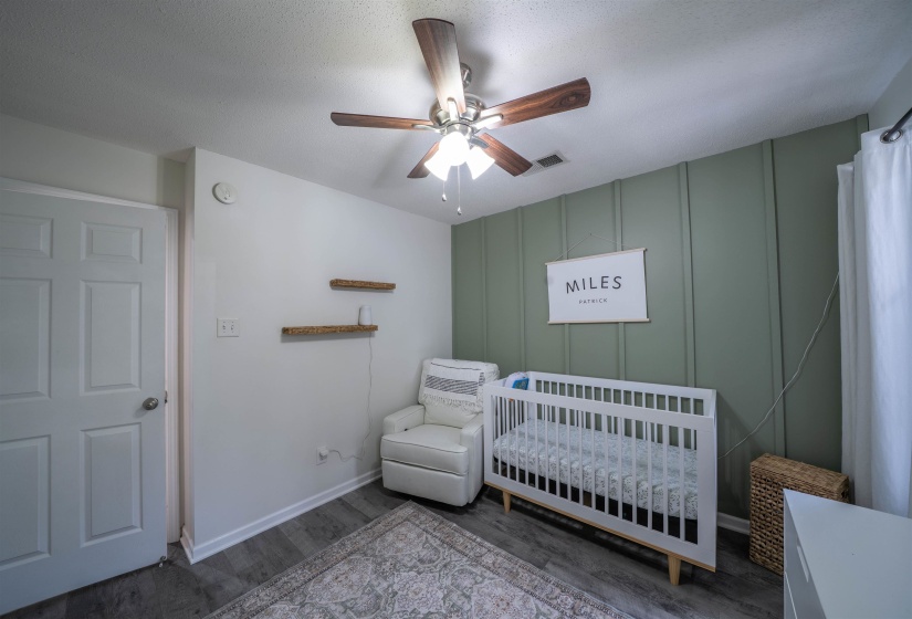 Bedroom featuring a decorative wall, a crib, wood finished floors, ceiling fan, and a textured ceiling