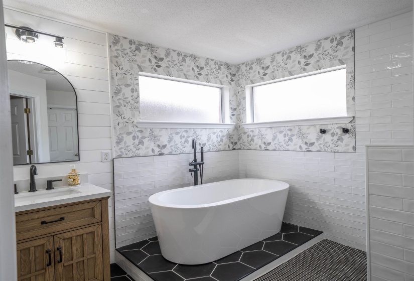 Bathroom with tile walls, a textured ceiling, vanity, a soaking tub, and a wainscoted wall