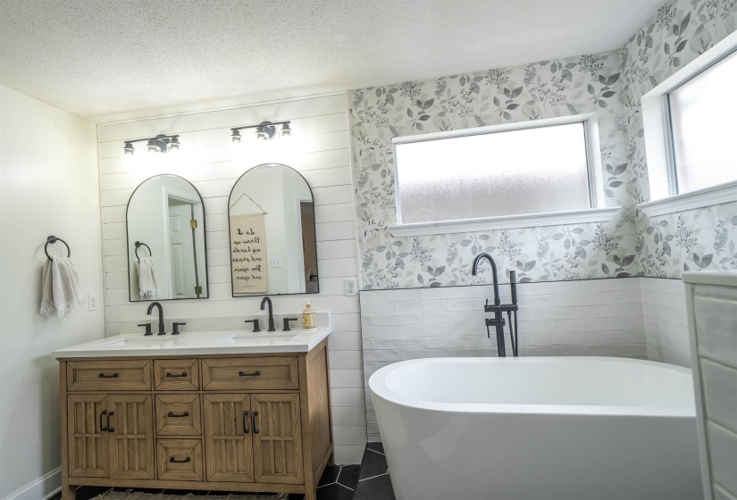 Bathroom with double vanity, tile walls, wainscoting, a textured ceiling, and a freestanding tub