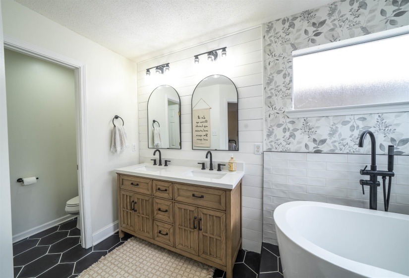 Full bathroom with double vanity, tile walls, a textured ceiling, a freestanding tub, and a wainscoted wall