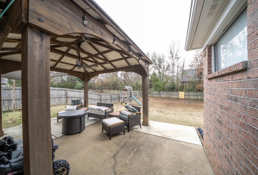 Fenced backyard with an outdoor living space, a gazebo, a patio area, a playground, and a ceiling fan