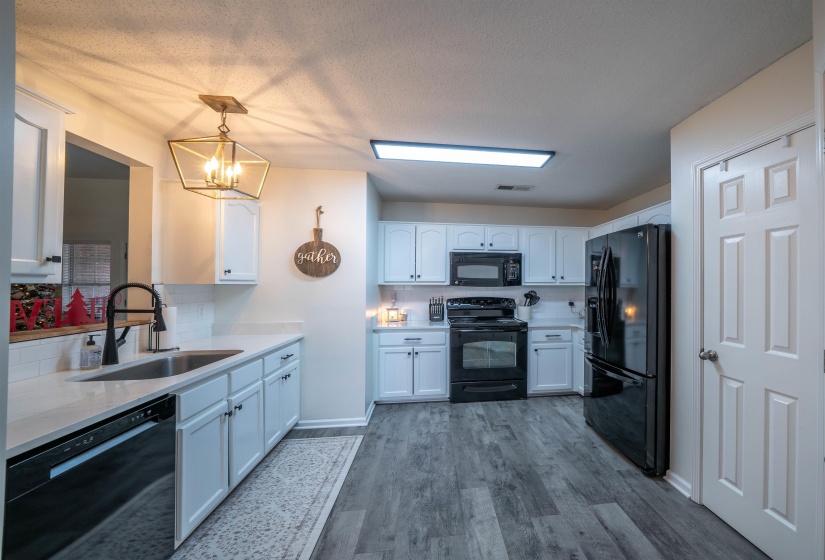 Kitchen with white cabinets, black appliances, pendant lighting, dark wood-type flooring, and light stone counters