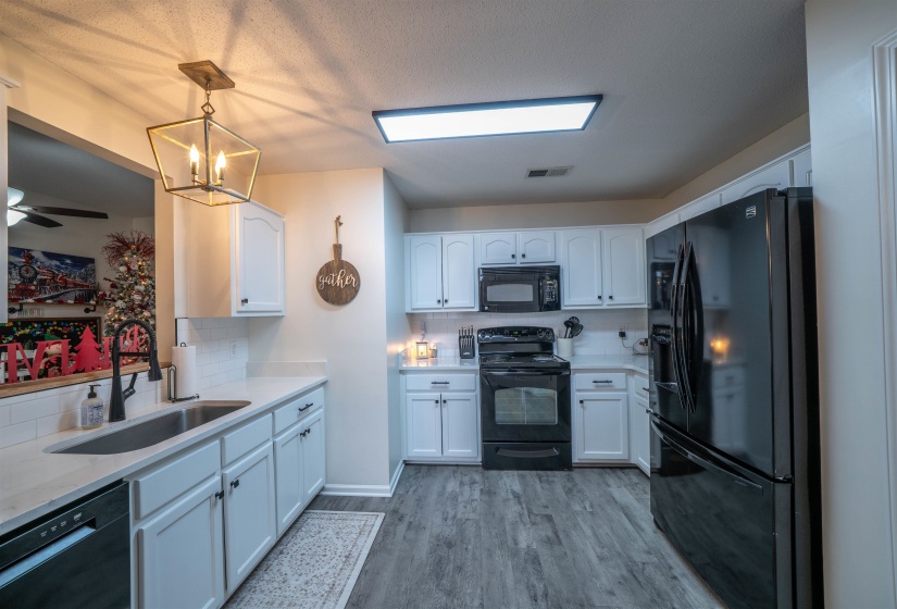 Kitchen featuring black appliances, white cabinets, tasteful backsplash, light stone countertops, and pendant lighting
