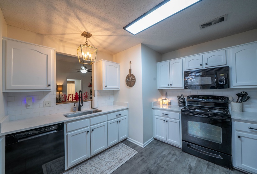 Kitchen featuring black appliances, white cabinetry, decorative backsplash, decorative light fixtures, and a textured ceiling