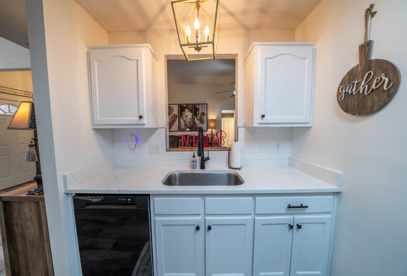 Kitchen featuring white cabinets, backsplash, black dishwasher, and light stone countertops
