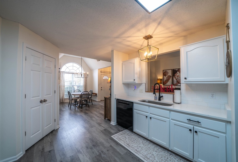 Kitchen with white cabinets, a chandelier, pendant lighting, dishwasher, and lofted ceiling
