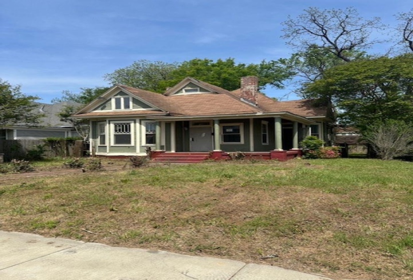 View of front of house featuring covered porch, a chimney, and a front yard