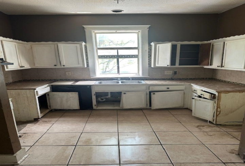 Kitchen featuring tasteful backsplash, light tile patterned flooring, white cabinets, and a textured ceiling