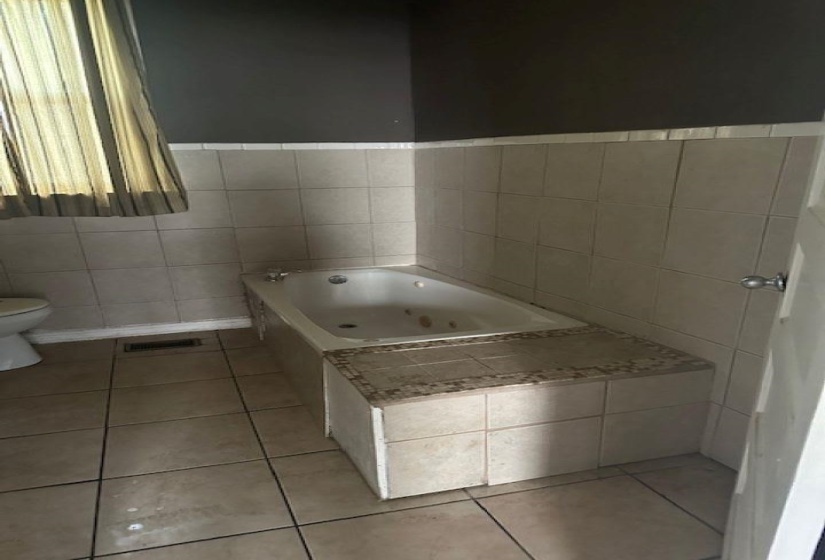 Bathroom with a tub with jets, light tile patterned floors, and tile walls