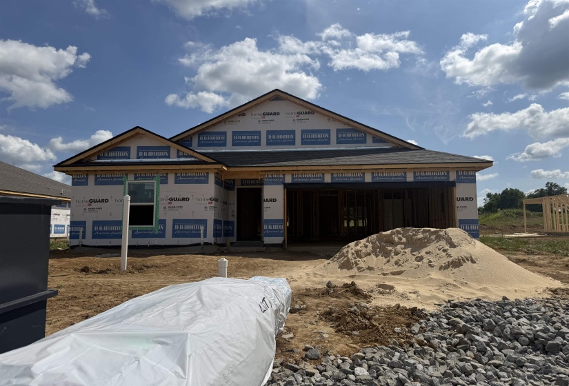 New construction home in framing stage, featuring a partial roof with dark shingles and exposed wood framing