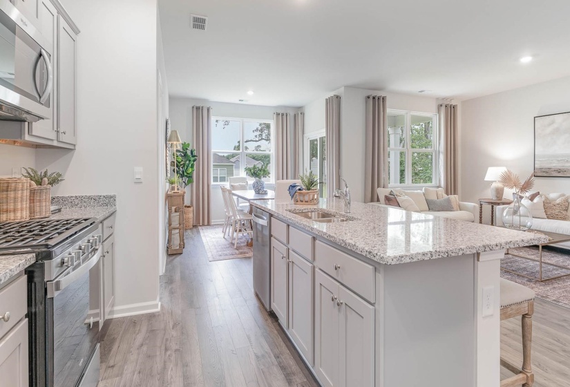 Kitchen featuring stainless steel appliances, light wood-style floors, light stone countertops, open floor plan, and a kitchen island with sink