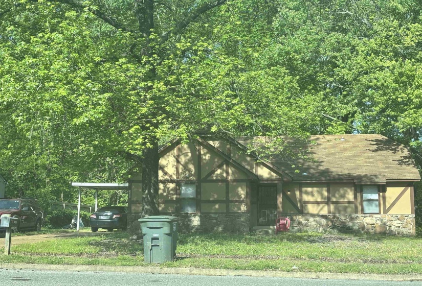 View of front of house featuring stone siding, a carport, roof with shingles, and a front lawn