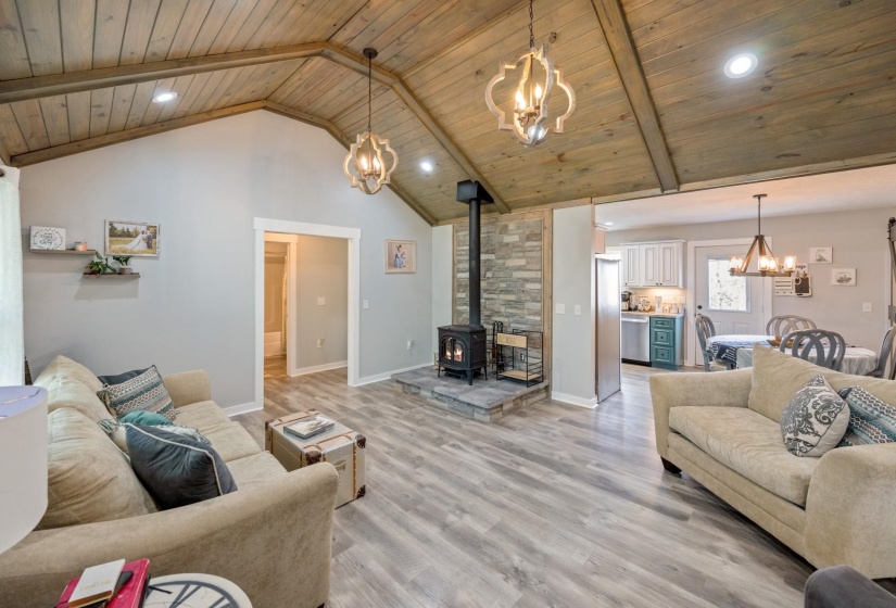 Living area featuring suspended lighting, a wood stove, a high wooden beamed ceiling, and light wood-type flooring