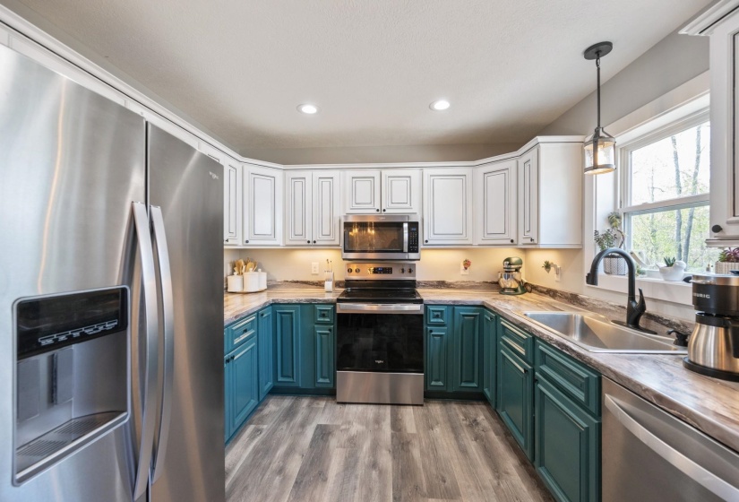 Kitchen featuring dual tone cabinets, stainless steel appliances, light countertops, hanging light fixtures, and light wood finished floors
