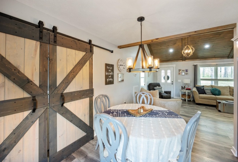 Dining room featuring lofted ceiling with beams, a barn door, suspended lighting, wood ceiling, and wood finished floors