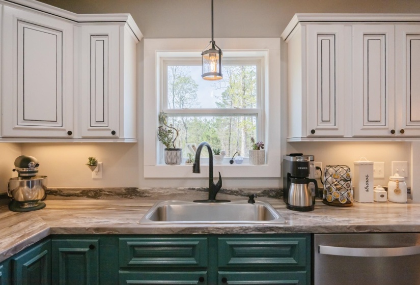 Two tone kitchen featuring two tone cabinetry, stainless steel dishwasher, decorative light fixtures, and light countertops