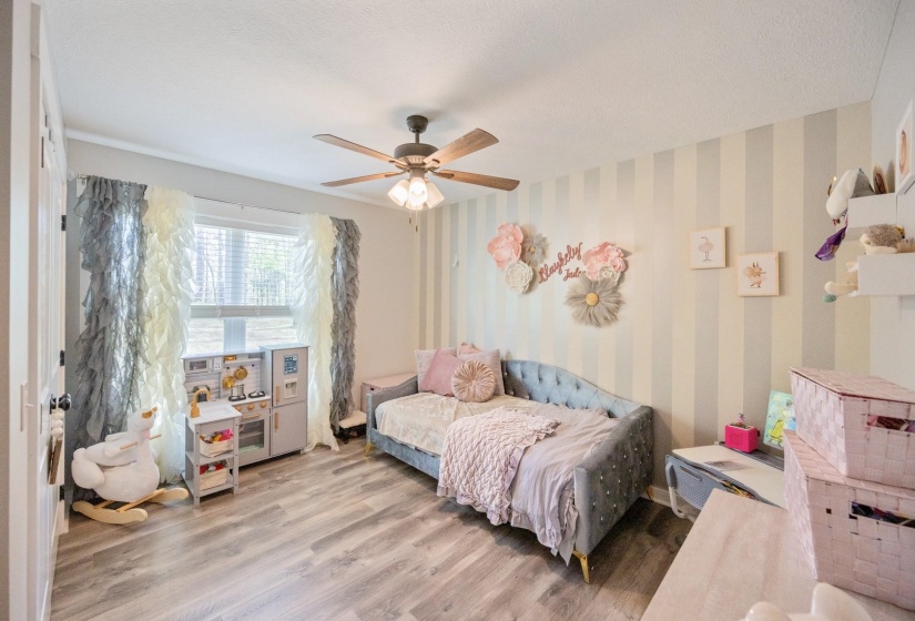 Bedroom with wood finished floors, wallpapered walls, a ceiling fan, and a textured ceiling