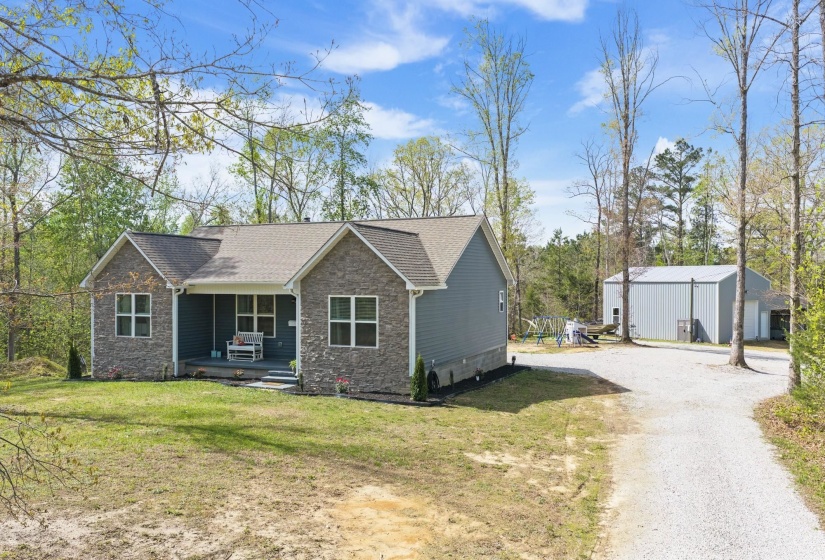 View of front of property with stone siding, covered porch, an outdoor structure, driveway, and roof with shingles