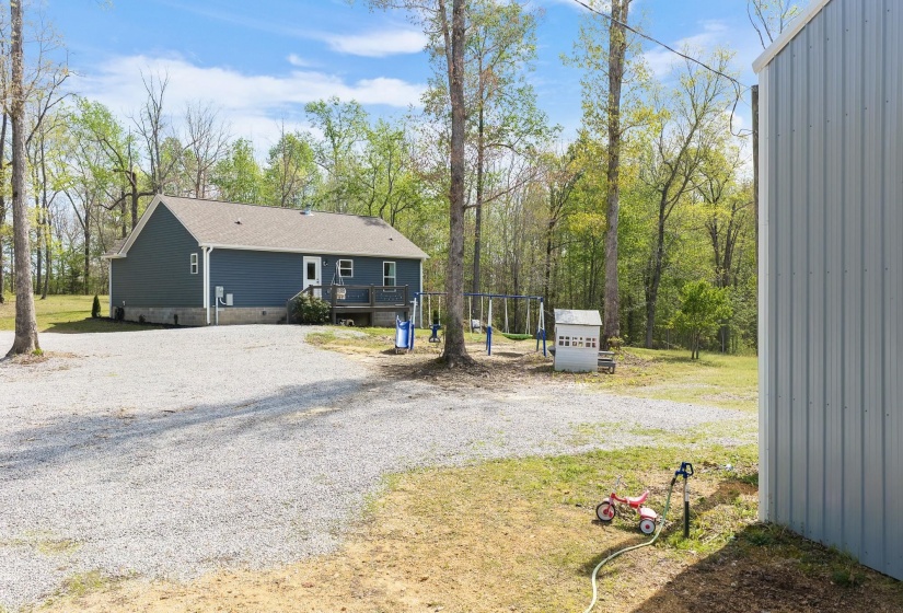 Rear view of house with a deck, gravel driveway, a playground, and view of scattered trees