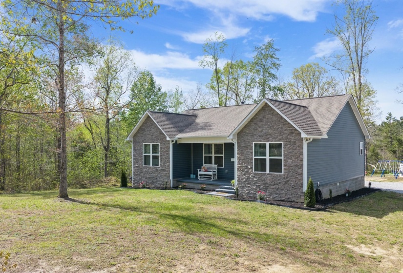 View of front of property featuring stone siding, a porch, a shingled roof, and a front yard