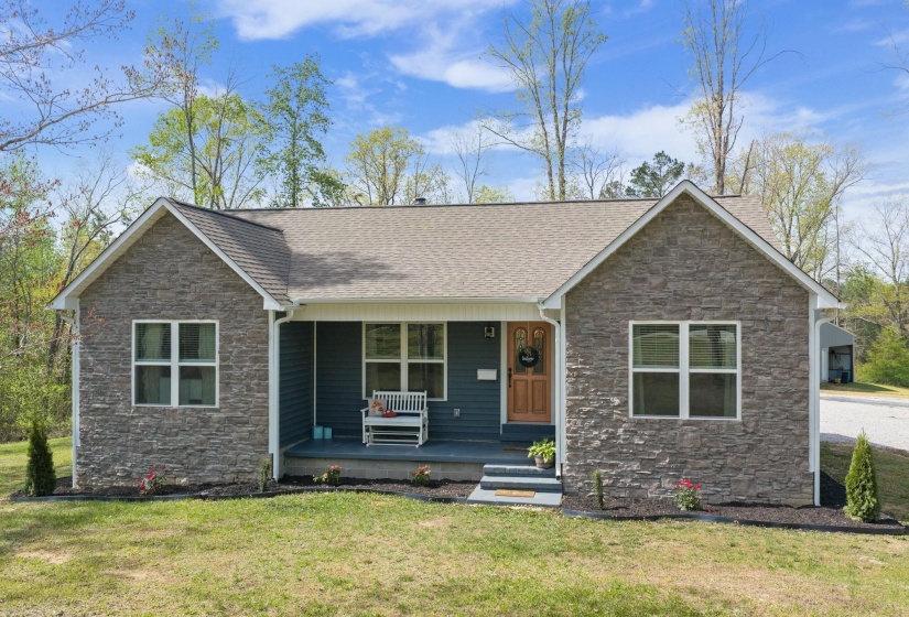 View of front facade featuring stone siding, covered porch, and a front yard