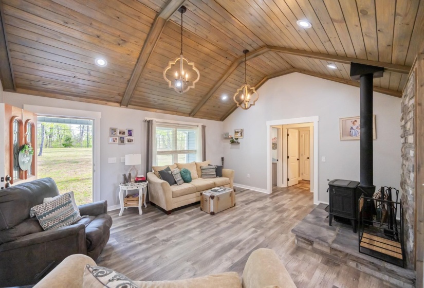 Living room featuring hanging lights, wood finished floors, a wood stove, and a high wooden beamed ceiling