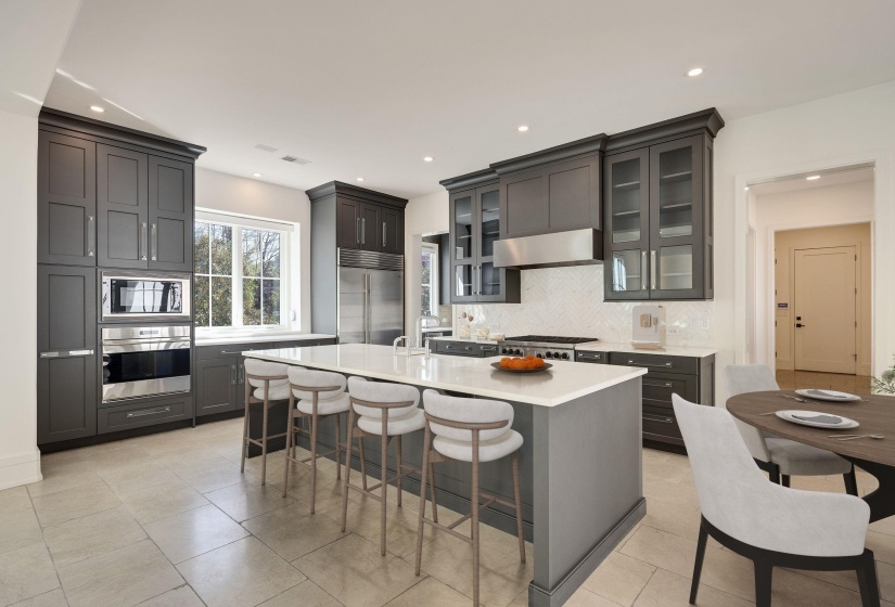 Kitchen featuring built in appliances, a breakfast bar area, light stone counters, a kitchen island with sink, and extractor fan