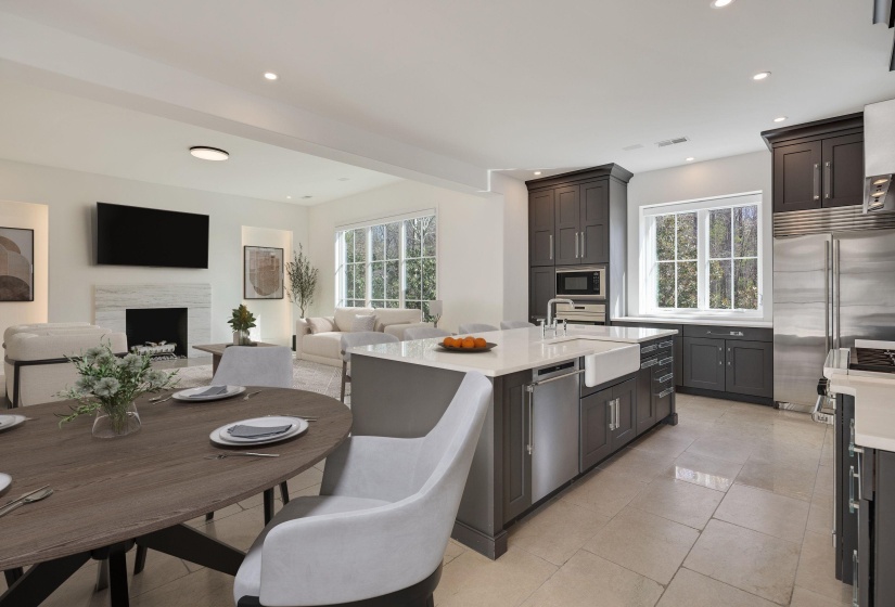Kitchen with open floor plan, light stone countertops, built in appliances, a center island with sink, and a fireplace