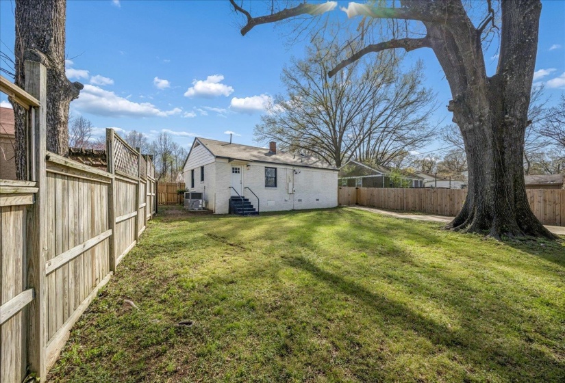 Rear view of house with a fenced backyard, entry steps, a chimney, and brick siding