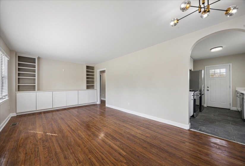 Empty room with arched walkways, built in shelves, dark wood-style floors, and a chandelier