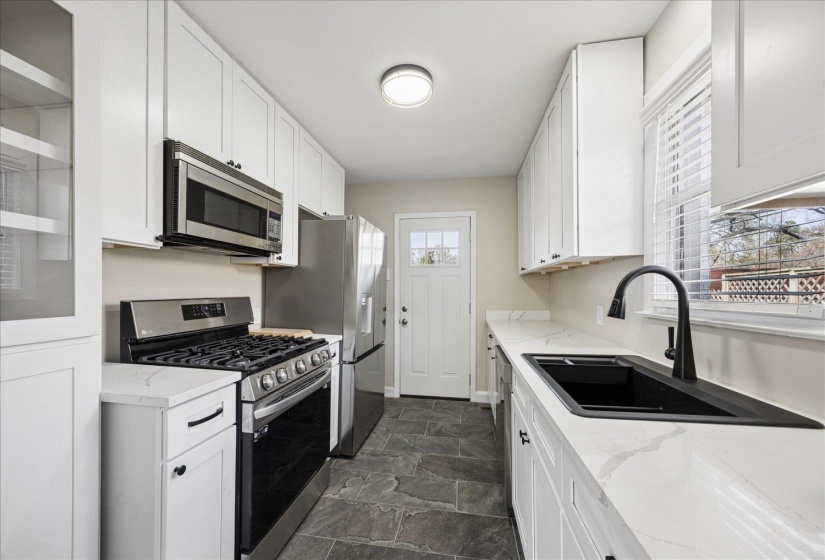 Kitchen with stainless steel appliances, white cabinets, stone finish floors, and light stone countertops