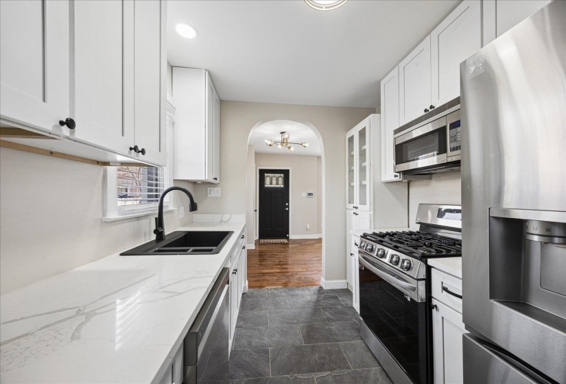 Kitchen featuring stainless steel appliances, white cabinets, arched walkways, light stone counters, and glass fronted cabinets
