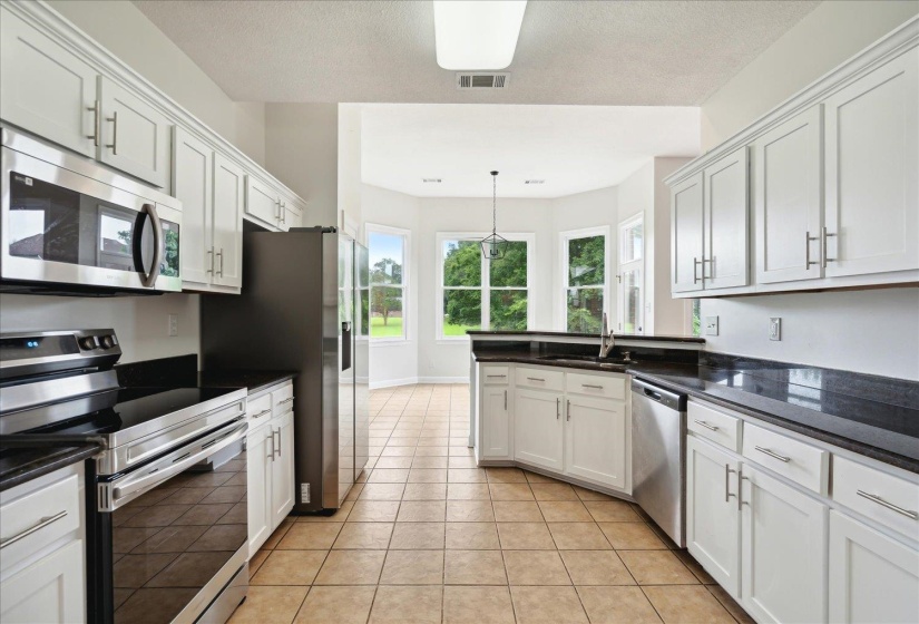 Kitchen with light tile patterned flooring, stove, dishwasher, and white cabinets