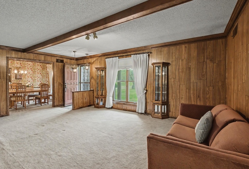 Living room featuring a textured ceiling, wooden walls, light carpet, and beam ceiling