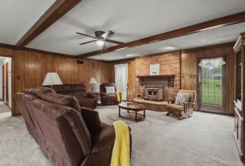 Living room featuring a textured ceiling, wood walls, beamed ceiling, light carpet, and ceiling fan