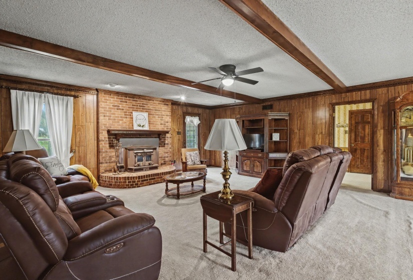 Living area featuring a textured ceiling, carpet floors, beamed ceiling, wooden walls, and a ceiling fan