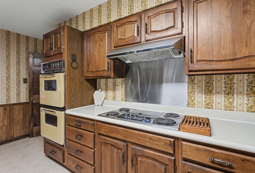 Kitchen with wallpapered walls, light countertops, a wainscoted wall, stainless steel electric cooktop, and a textured ceiling