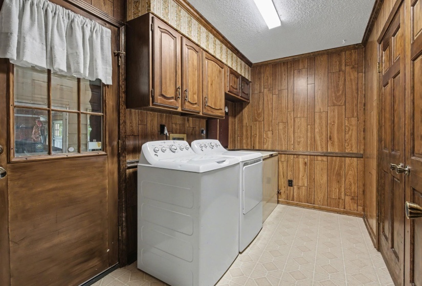 Laundry area featuring wood walls, a textured ceiling, washing machine and clothes dryer, light flooring, and cabinet space