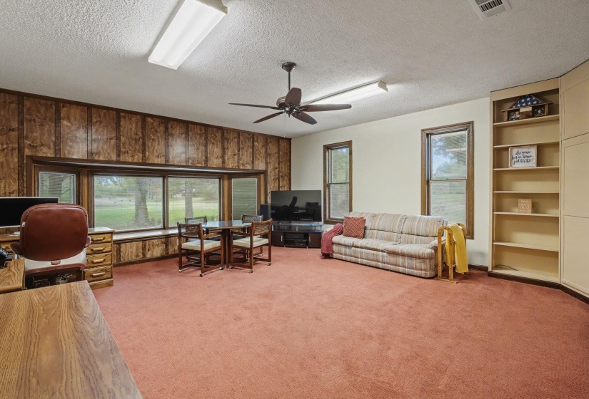 Living area featuring wooden walls, light colored carpet, a textured ceiling, a ceiling fan, and built in features