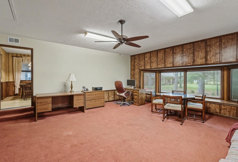 Home office featuring wood walls, light colored carpet, a ceiling fan, and a textured ceiling